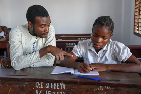 Un adulte assis à côté d’une élève lui montre une ligne de son cahier.