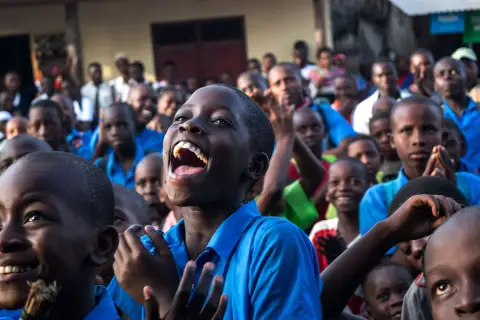 Des enfants rient aux éclats, serrés les uns contre les autres dans une cour.