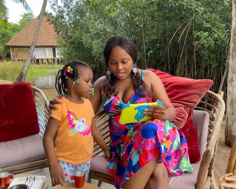 Une mère tient une tablette pour enfant, sa fille debout à côté d’elle, dans un jardin.